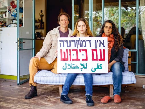 Sofia Orr et ses parents, chez eux, à Pardes Hanna. Sofia s’apprête à refuser en août 2023 de faire le service militaire. Elle a la chance – le « privilège », dit-elle – de bénéficier du soutien de ses parents. Sur la pancarte, en hébreu : « Il n’y a pas de démocratie sous occupation », et en arabe (ligne du dessous) : « Assez avec l’occupation ». Photo : Haidi Motola pour La Déferlante